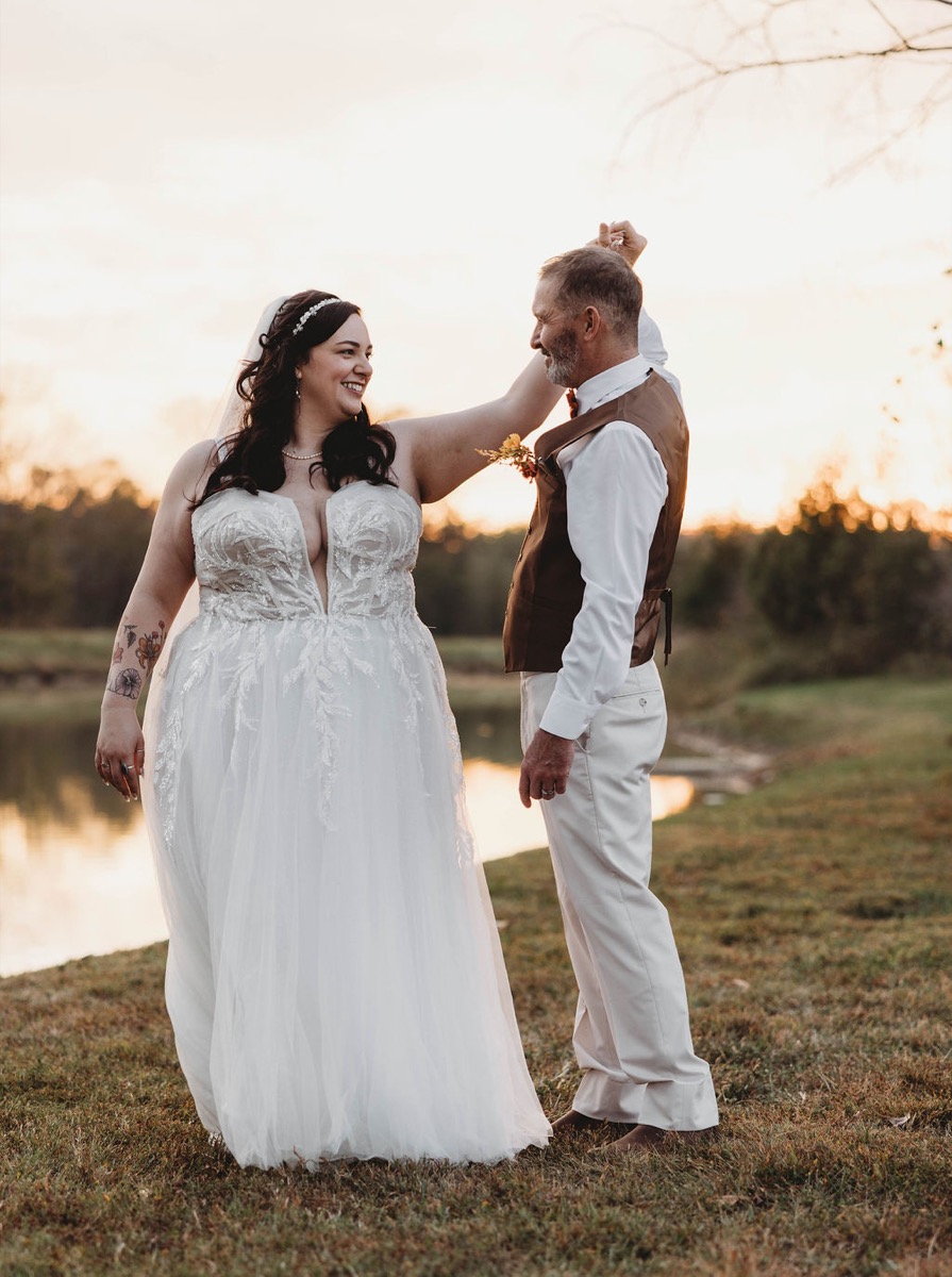 Tori & Tim dance hand-in-hand beside the Pond at golden-hour sunset in lace gown and vest at Covey Creek