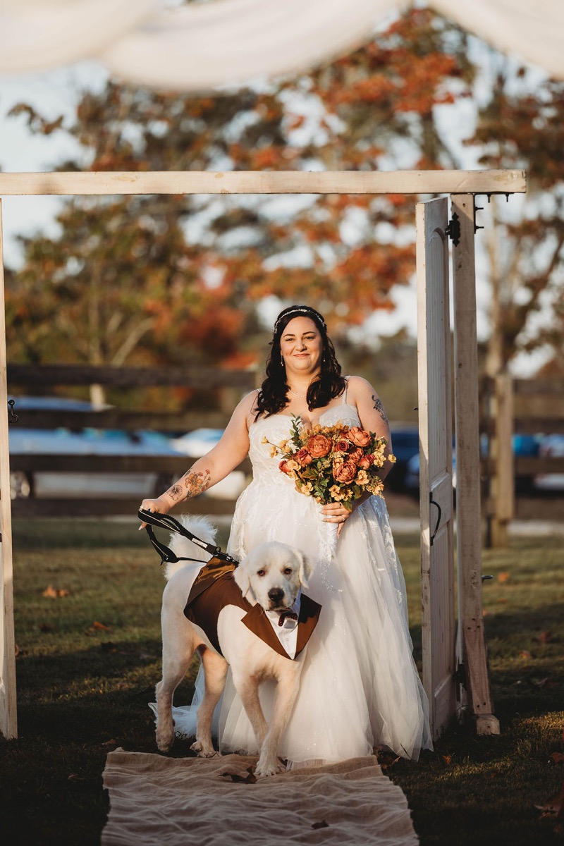 Tori holds an autumn bouquet and her dog's leash at the outdoor ceremony entrance at Covey Creek
