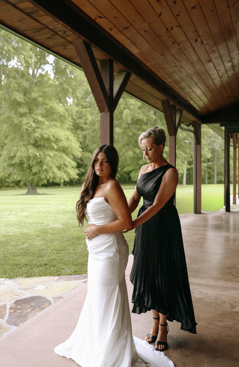 A bridesmaid in black adjusts Cadence's gown on the porch before Cadence & Brody's day at Covey Creek