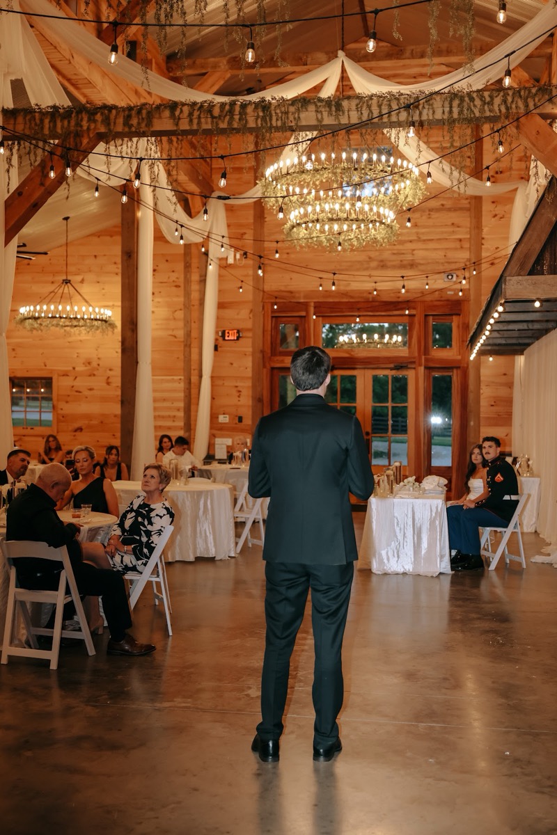 A toast unfolds in the draped barn as Cadence & Brody sit at their sweetheart table at Covey Creek