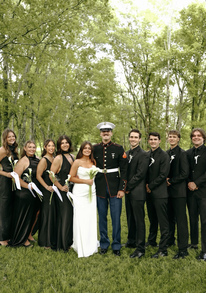 Cadence & Brody stand with their black-clad wedding party and white calla lilies on the lawn at Covey Creek
