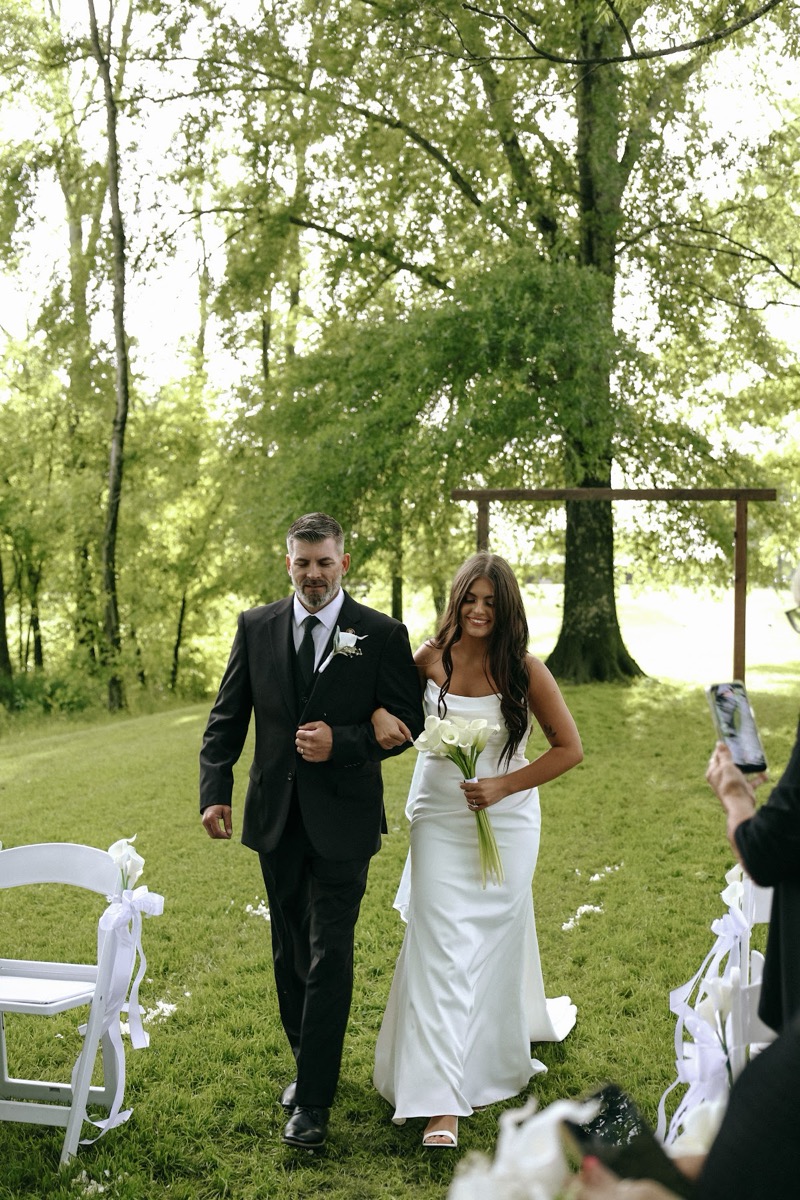 Cadence walks the aisle on her father's arm with calla lilies at Cadence & Brody's Covey Creek ceremony