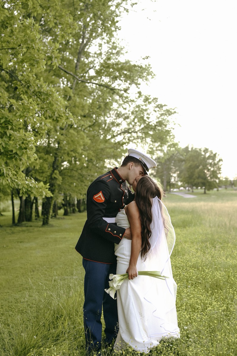 Cadence & Brody kiss in tall grass under leafy trees, calla lilies in her hand, at Covey Creek