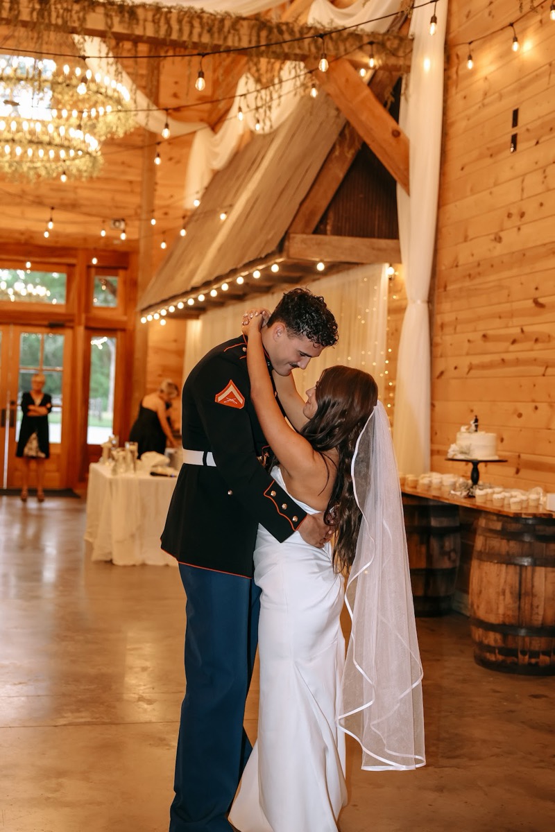 Cadence & Brody smile through their first dance under barn chandeliers beside the cake at Covey Creek