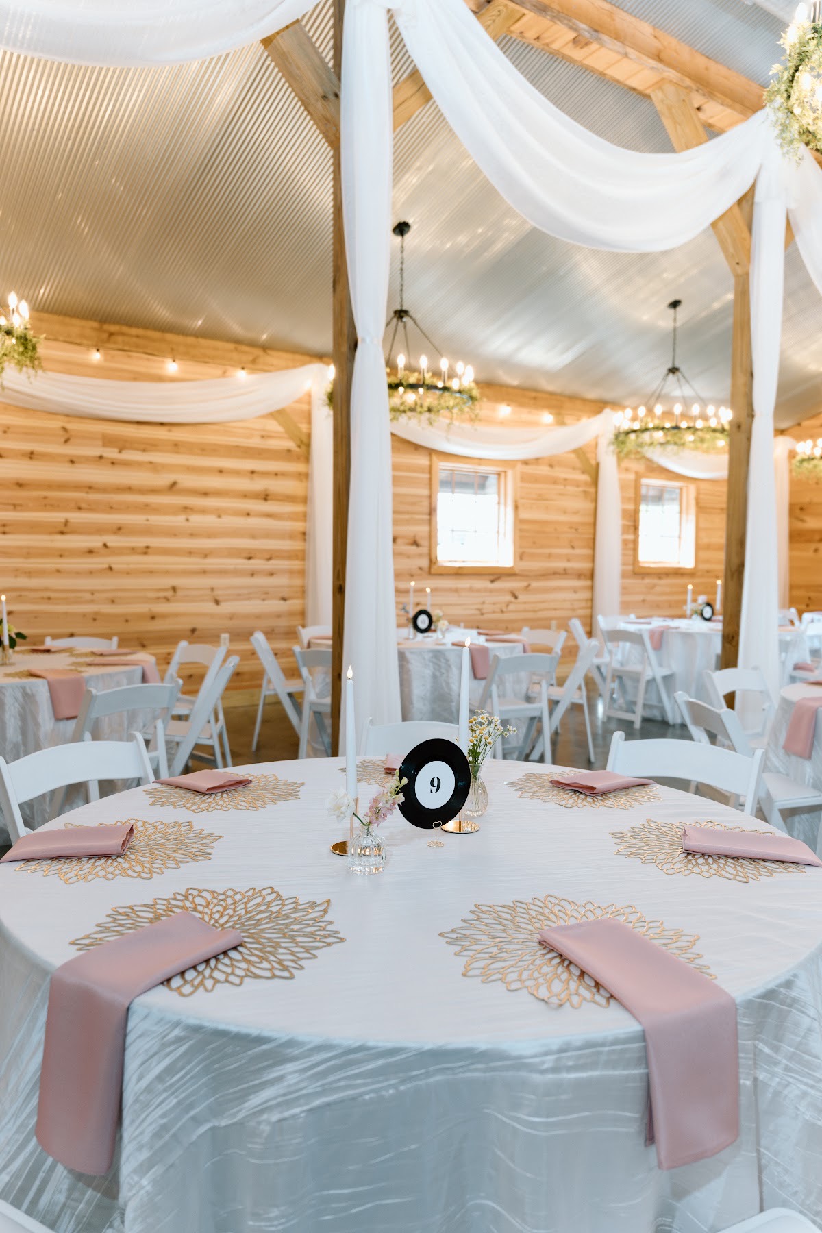 Table nine with gold placemats, mauve napkins, and a vinyl number waits in the barn for Katelynn & Justin at Covey Creek