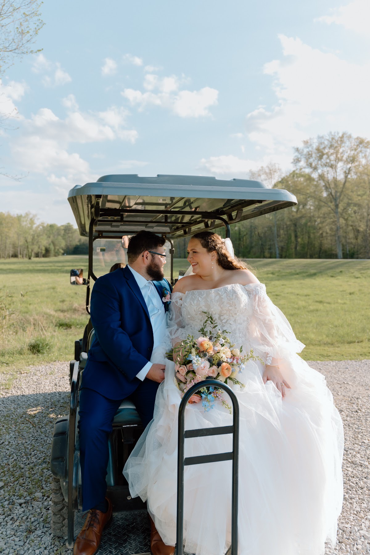 Katelynn & Justin smile at each other on a golf cart overlooking green fields at Covey Creek
