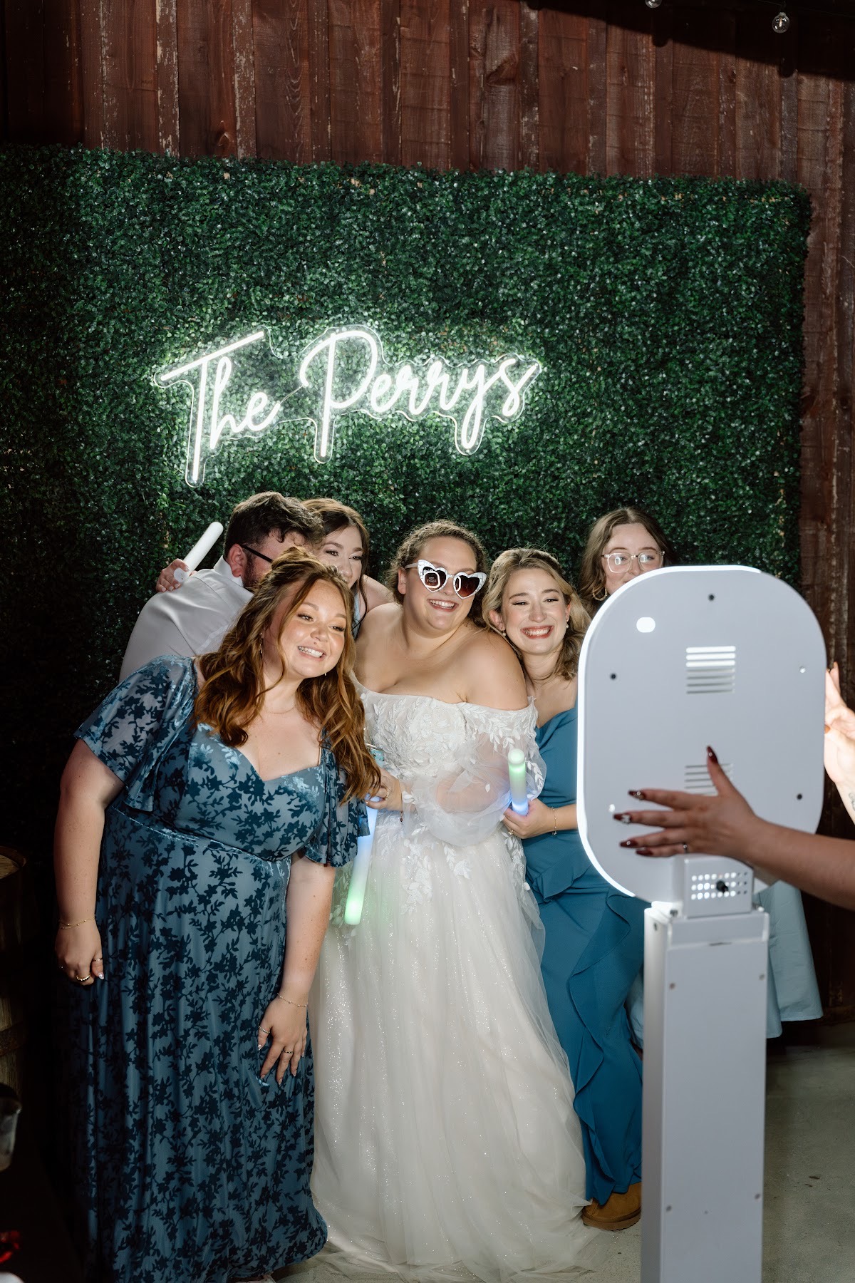 Katelynn & Justin's guests pose with the bride at a photo booth under a neon sign in the barn at Covey Creek