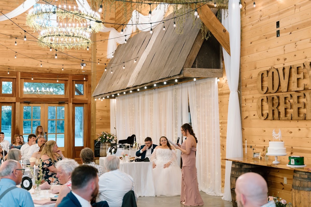 A bridesmaid toasts Katelynn & Justin at the head table beneath Covey Creek wall letters in the barn