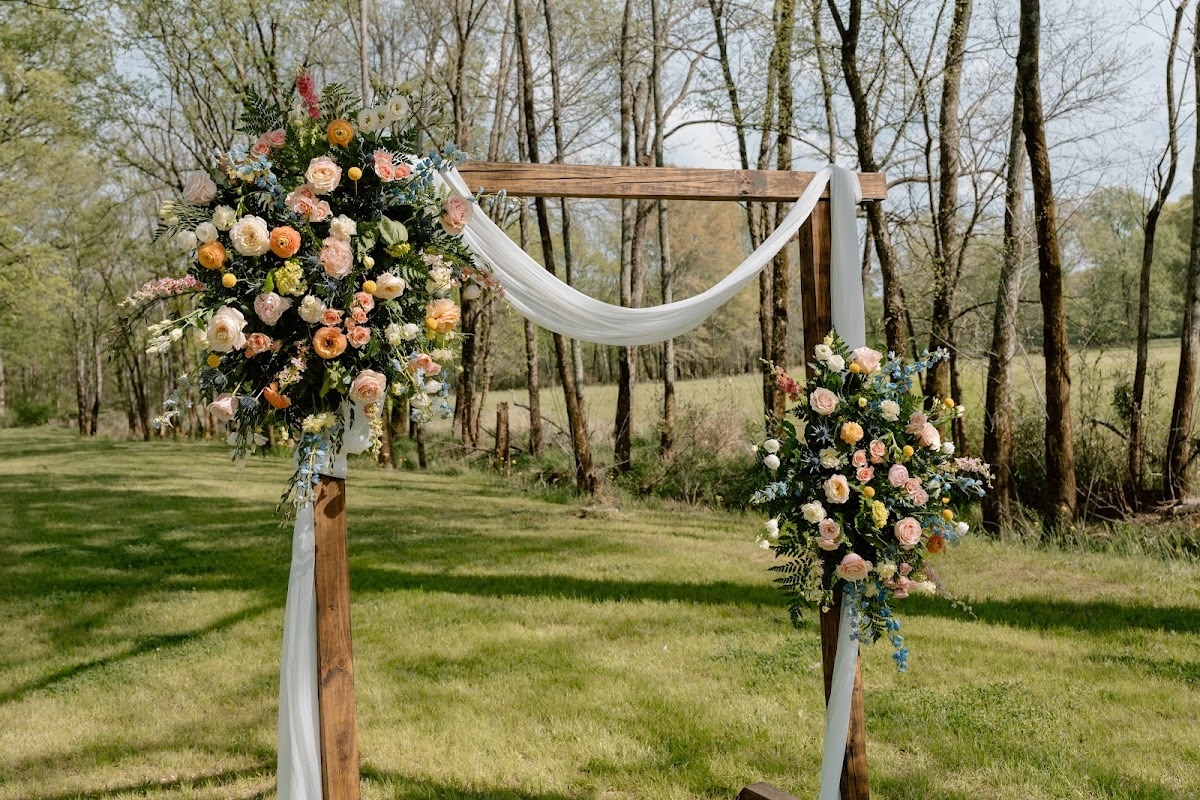 A floral wooden ceremony arbor with white draping stands in a grassy field for Katelynn & Justin at Covey Creek