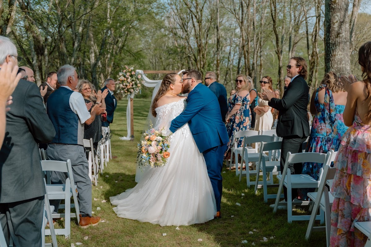 Katelynn & Justin share a kiss in the grassy aisle as guests clap after their outdoor ceremony at Covey Creek