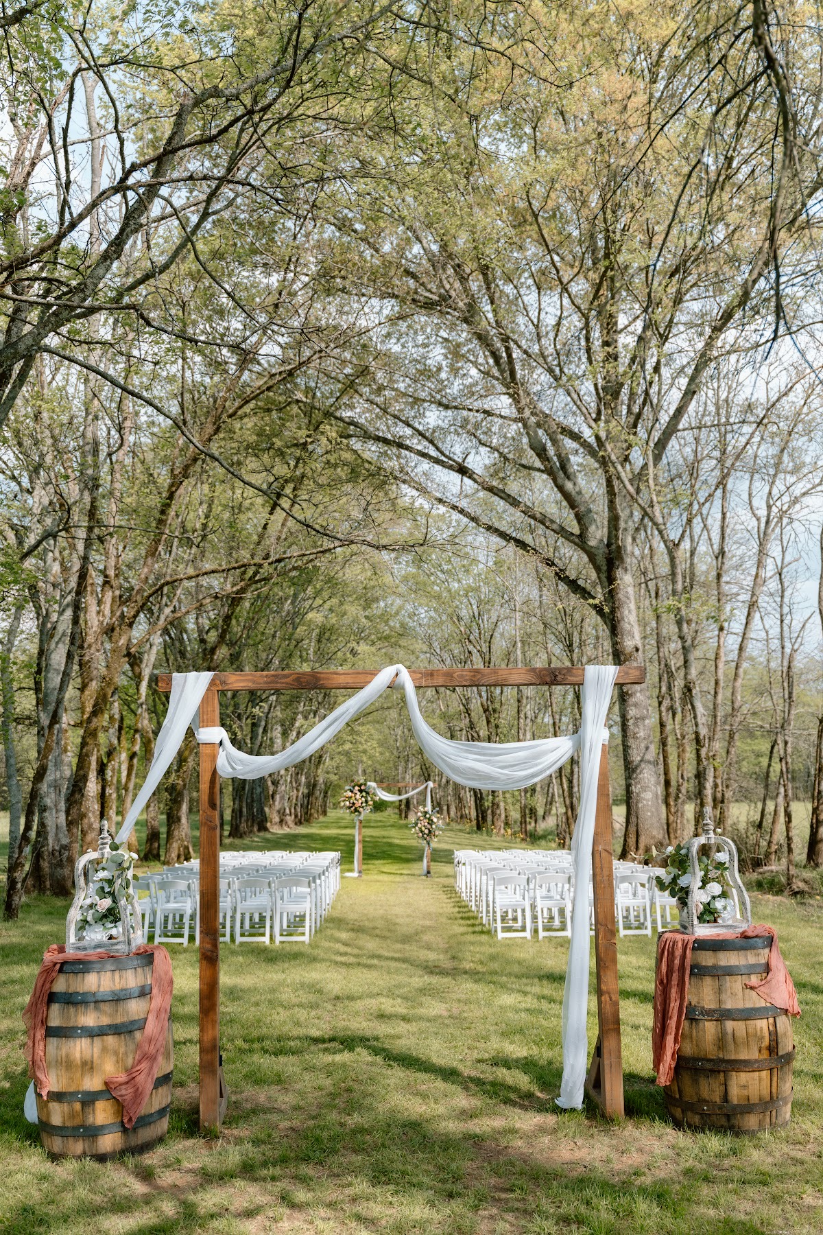 White chairs line the Tunnel of Love aisle under trees for Katelynn & Justin's outdoor ceremony at Covey Creek