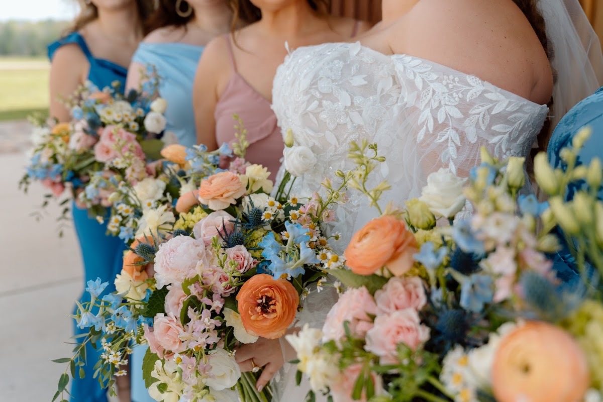 Katelynn & Justin's bridal party holds peach, pink, and blue bouquets in a waist-up lineup outdoors at Covey Creek