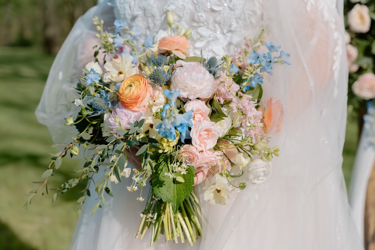 Katelynn & Justin's peach, pink, and blue bridal bouquet rests against her lace gown outdoors at Covey Creek