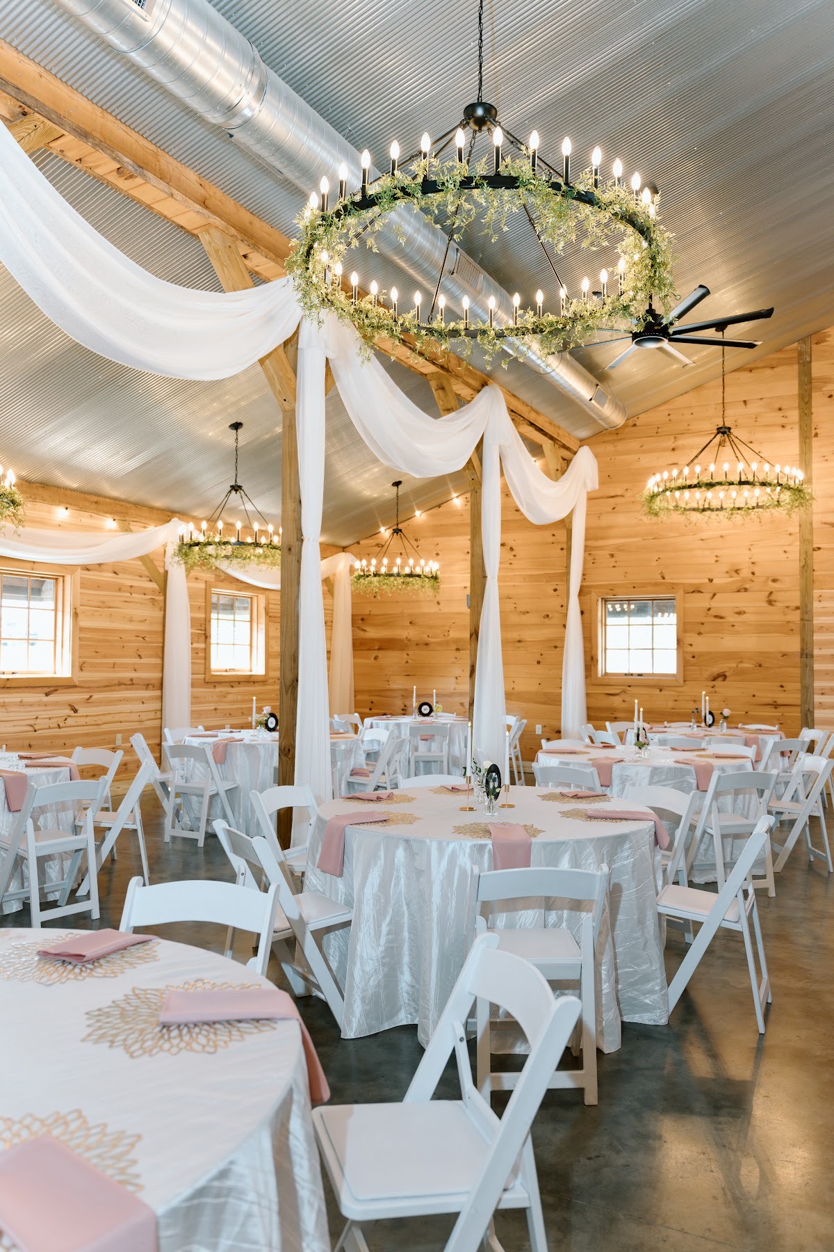 Round tables with gold placemats and wagon-wheel chandeliers fill the draped barn for Katelynn & Justin at Covey Creek