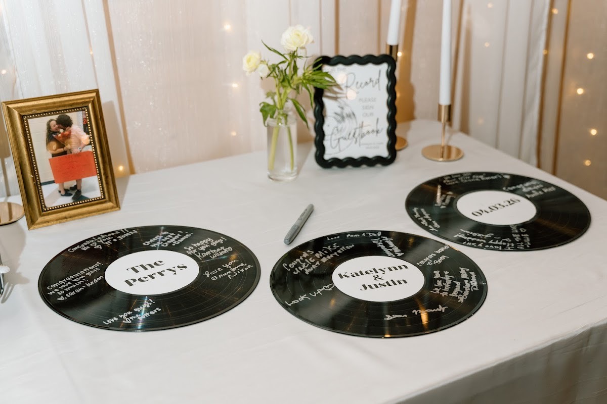 Vinyl guestbook records labeled Katelynn & Justin sit with candles and roses at their Covey Creek reception