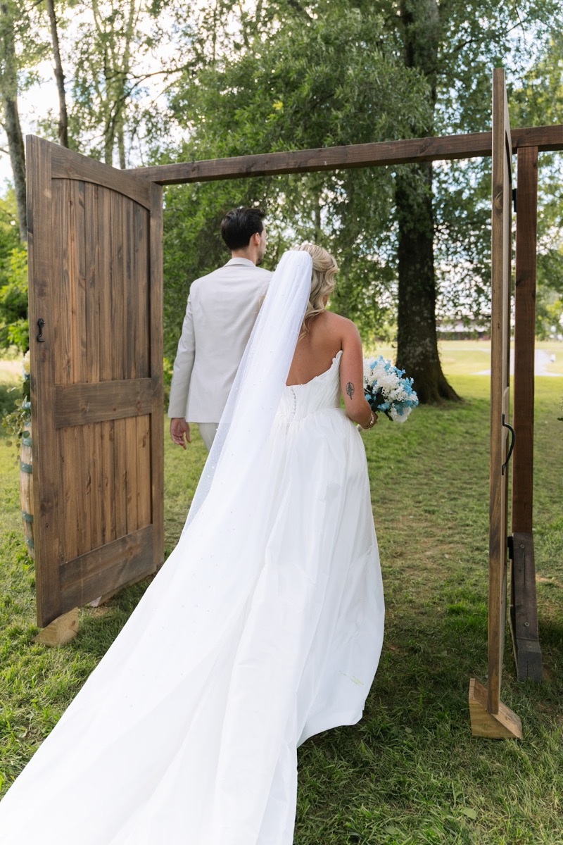 Kyley & Nick walk through open wooden doors onto the sunlit lawn for portraits at Covey Creek
