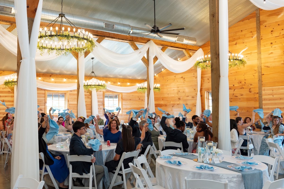 Guests wave light blue napkins under barn chandeliers at Kyley & Nick's reception at Covey Creek