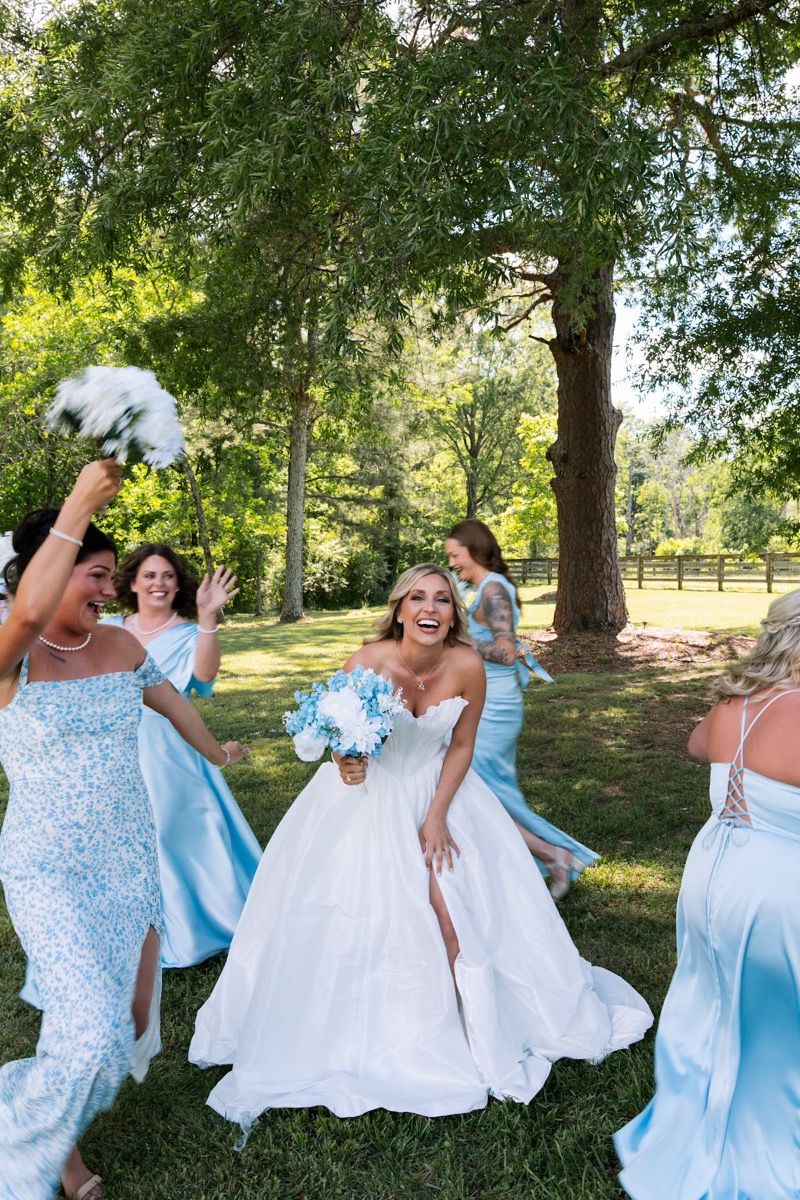 Kyley and bridesmaids cheer on the lawn with bouquets raised under trees for Kyley & Nick at Covey Creek