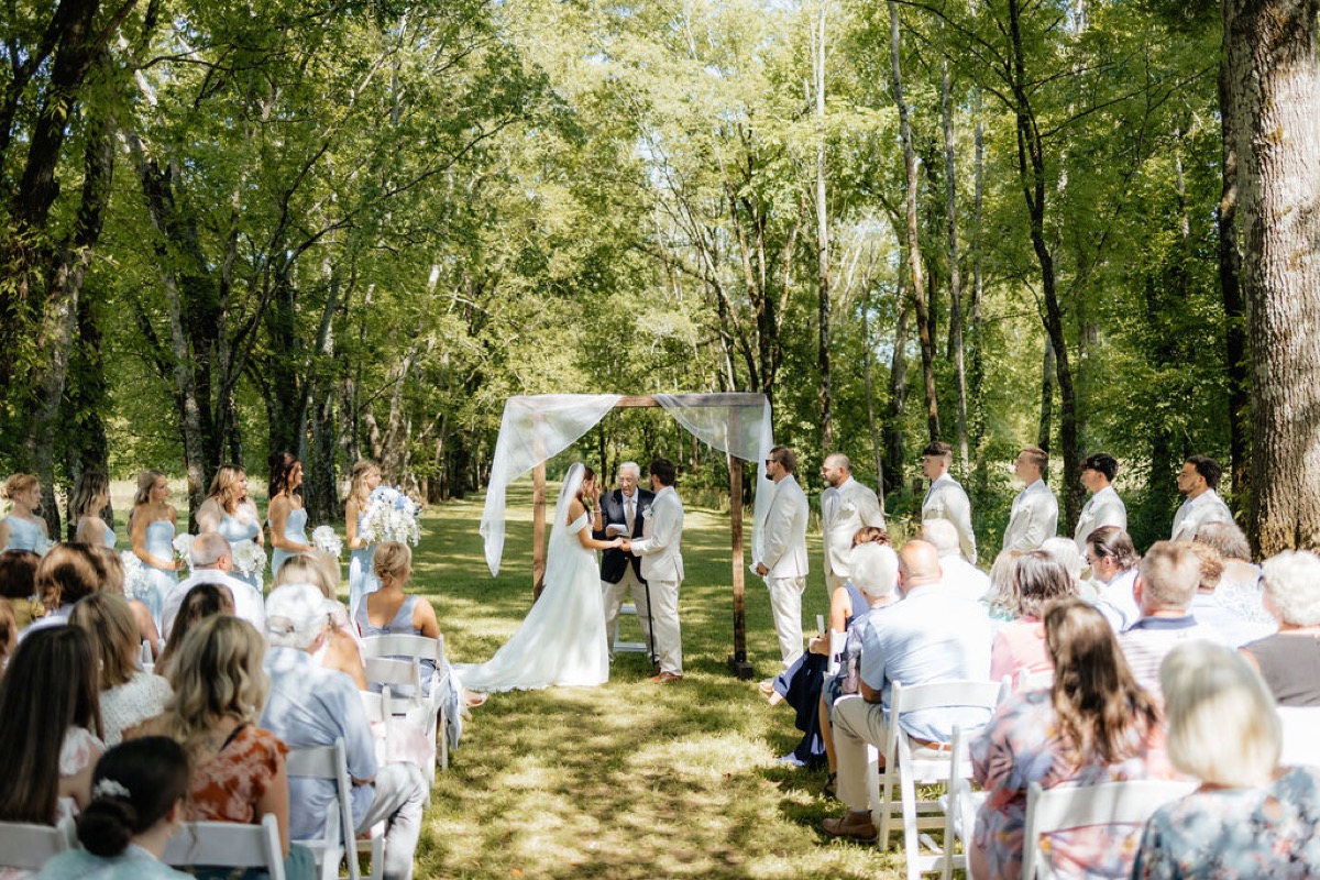 Kylie & Mason exchange vows under a wood arbor as guests watch the Tunnel of Love ceremony at Covey Creek