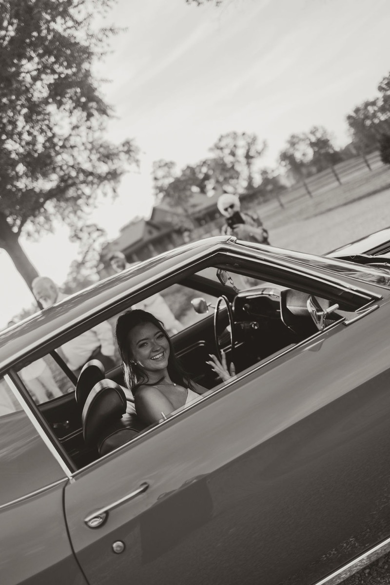 Kylie smiles from a vintage getaway car window at Covey Creek after Kylie & Mason’s spring wedding