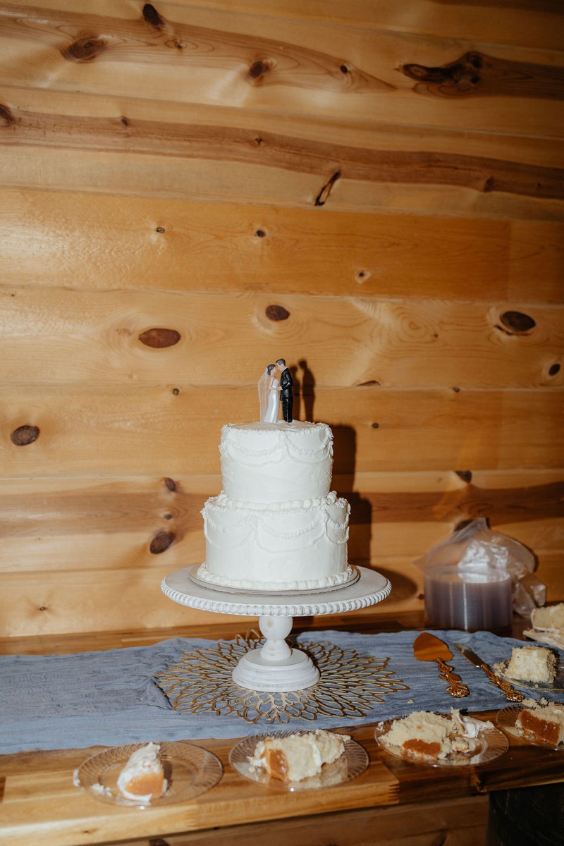 Two-tier white cake for Kylie & Mason with figurine topper against wood walls at Covey Creek indoor reception