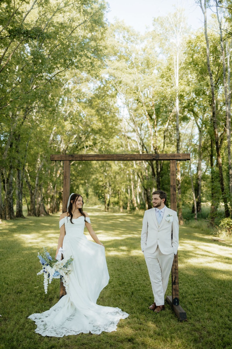 Kylie & Mason smile under a wood arbor along the Tunnel of Love tree canopy at Covey Creek in spring