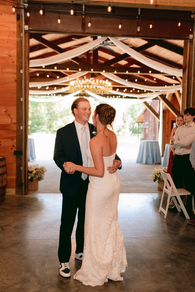 Rachel & Ben share a first dance in the draped indoor reception barn under string lights at Covey Creek.