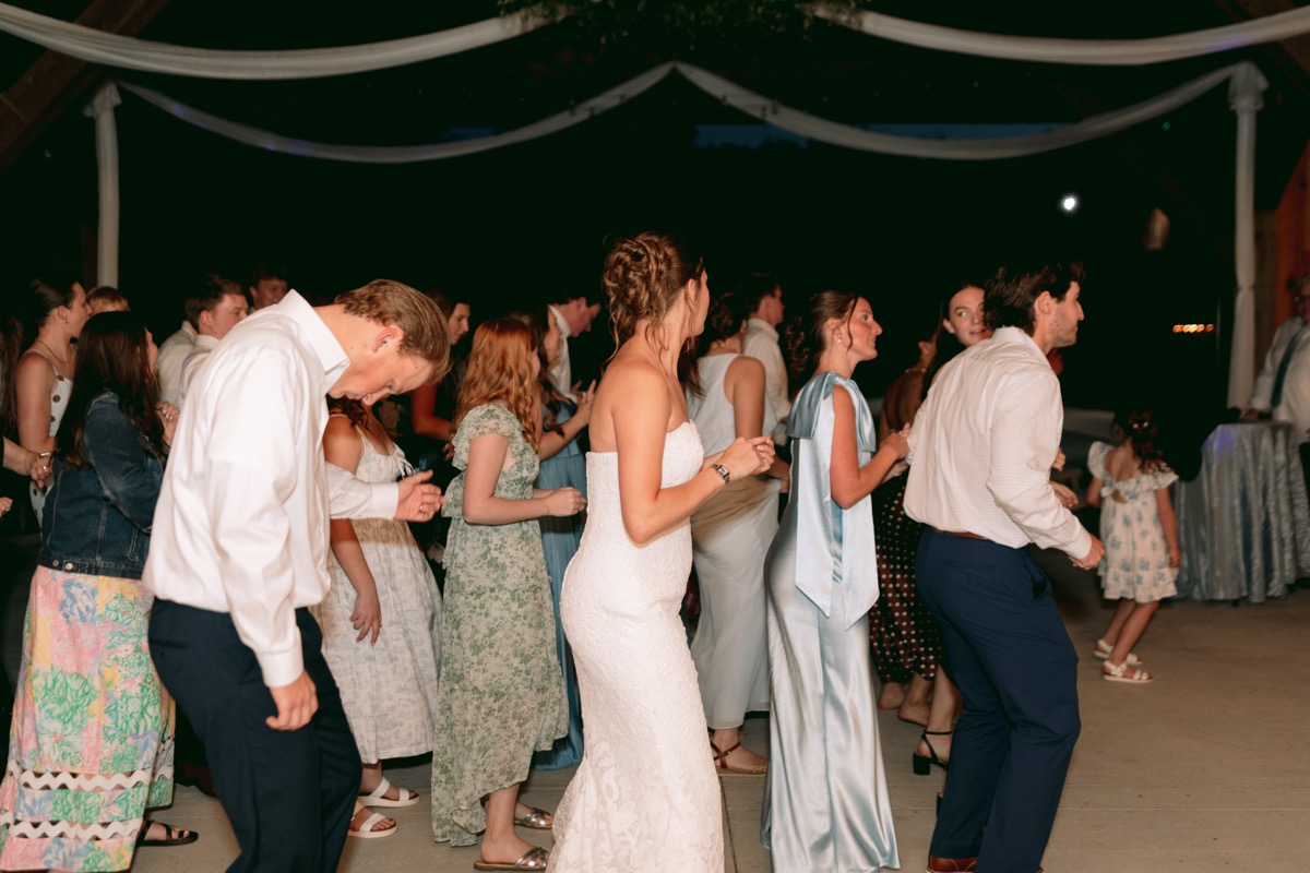 Rachel & Ben dance with guests on the indoor reception floor under draped fabric at Covey Creek.