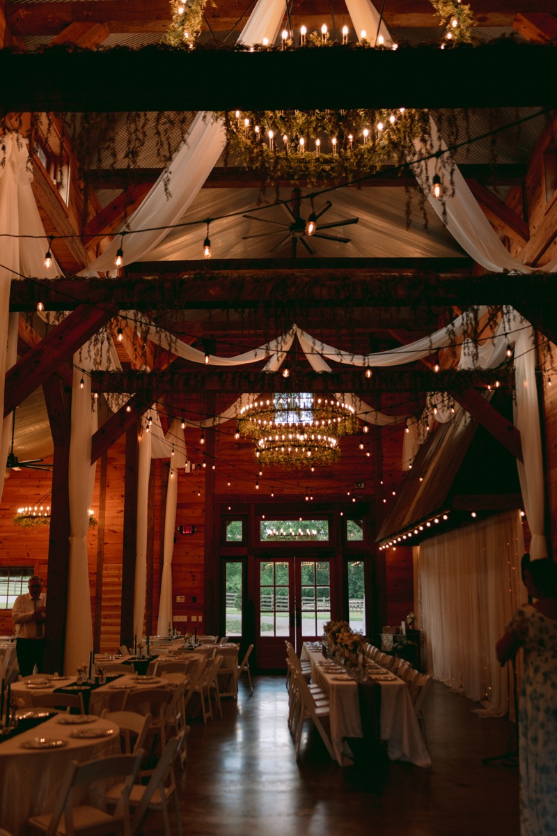 Rachel & Ben's indoor reception hall with draped ceilings, chandeliers, and set tables at Covey Creek.