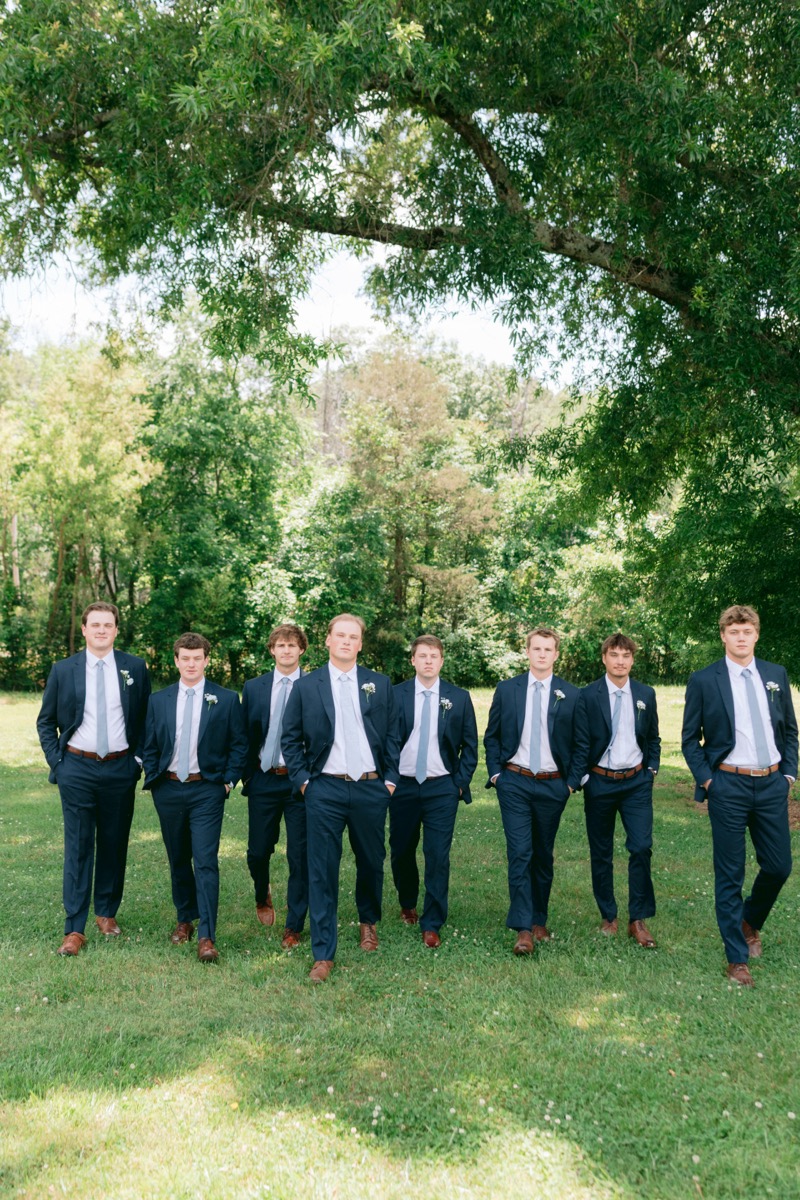 Rachel & Ben's groomsmen in navy suits walk under the Tunnel of Love canopy at Covey Creek.