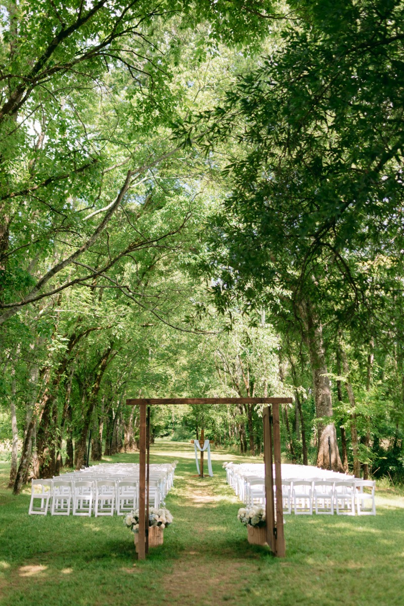 Rachel & Ben's Tunnel of Love ceremony setup with wooden arbor, white chairs, and cross at Covey Creek.