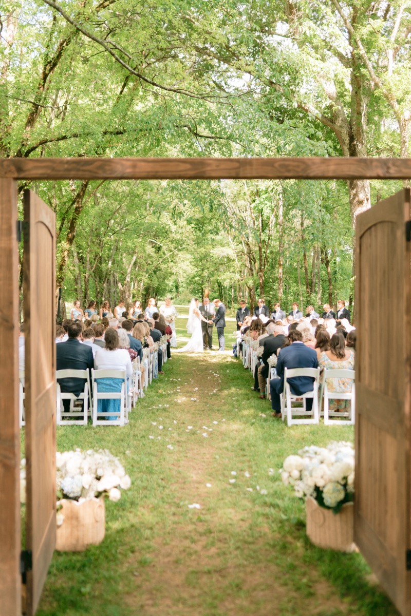 Rachel & Ben stand at the altar through open wooden doors under the Tunnel of Love at Covey Creek.
