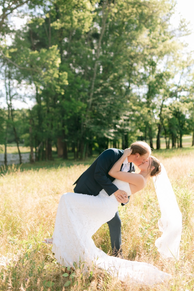 Rachel & Ben share a romantic dip kiss in a sunlit golden meadow on a spring day at Covey Creek.