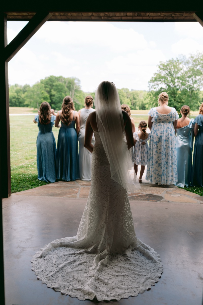 Rachel & Ben's bridal party in blue looks out from the patio over spring fields at Covey Creek.