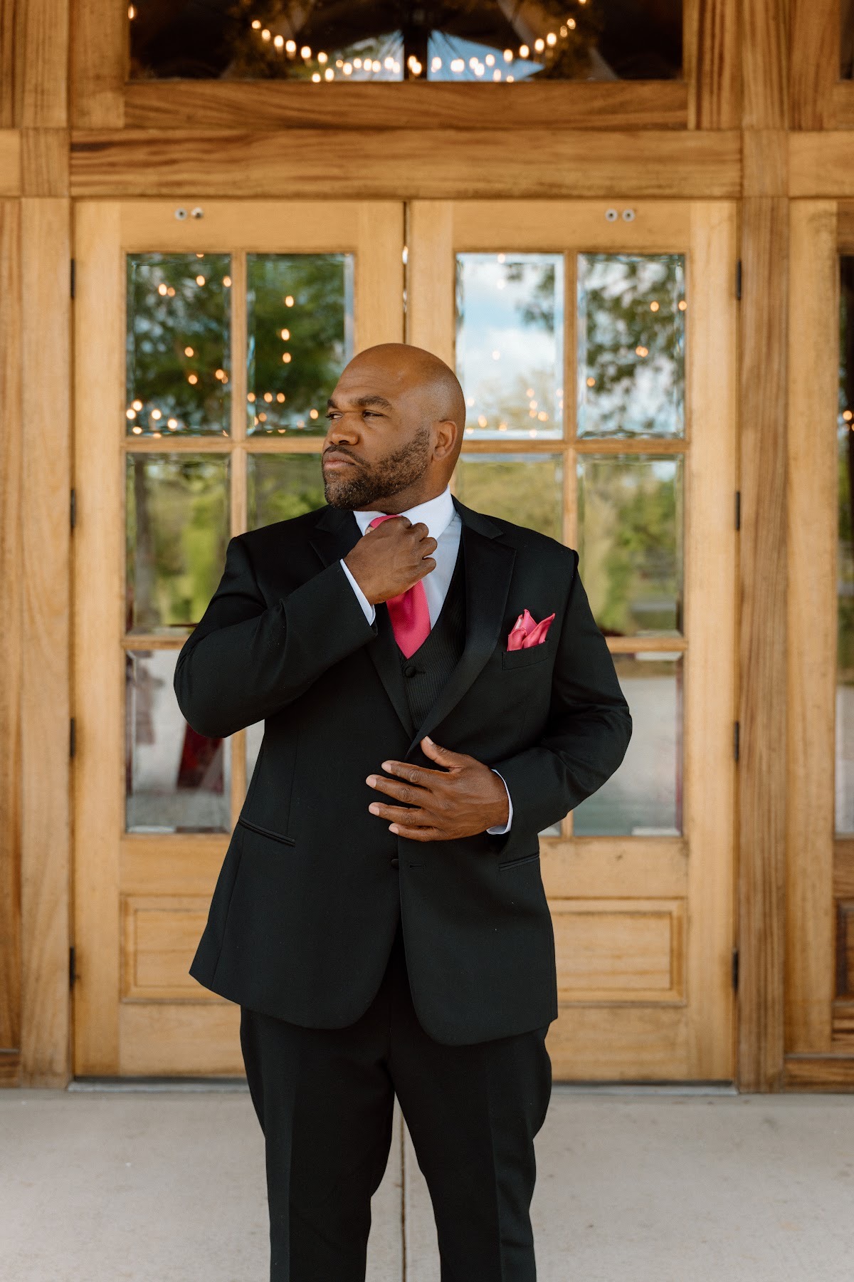 Josh adjusts his bright pink tie before the wooden barn doors for Stephanie & Josh at Covey Creek