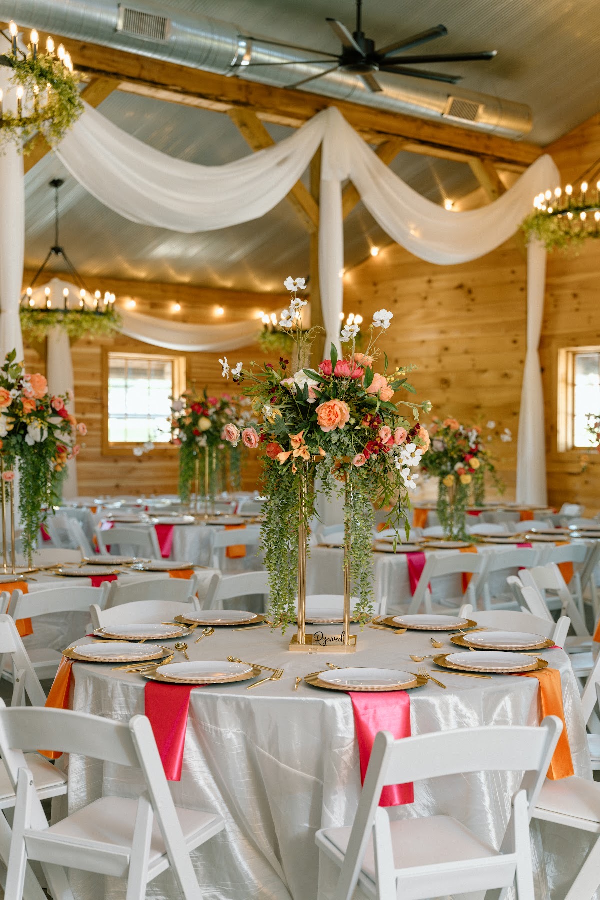 Reserved table with a tall gold floral and pink-orange napkins for Stephanie & Josh at Covey Creek