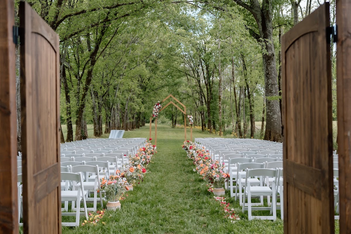 Empty flower-lined aisle framed by open wooden doors leads to the arch for Stephanie & Josh at Covey Creek