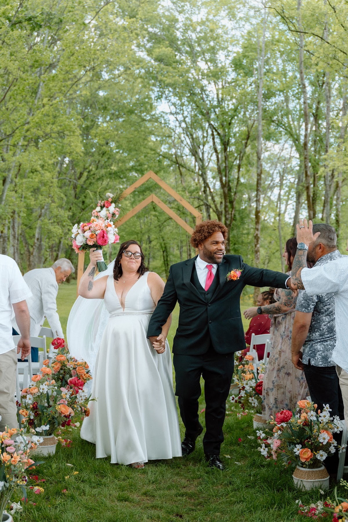 Stephanie & Josh walk the flower-lined aisle, bouquet raised as Josh high-fives guests at Covey Creek