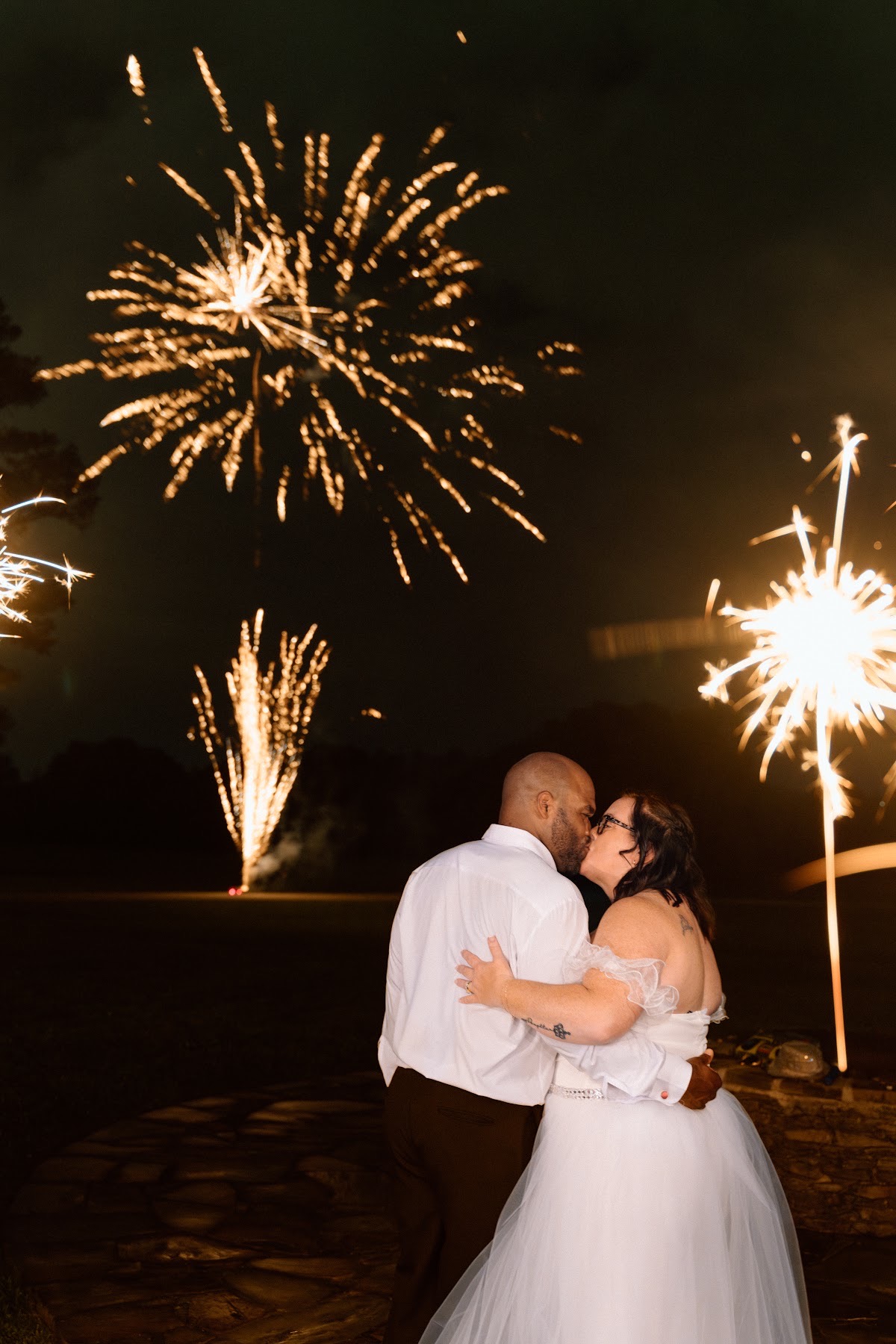 Stephanie & Josh kiss on the stone patio as golden fireworks burst above them at Covey Creek