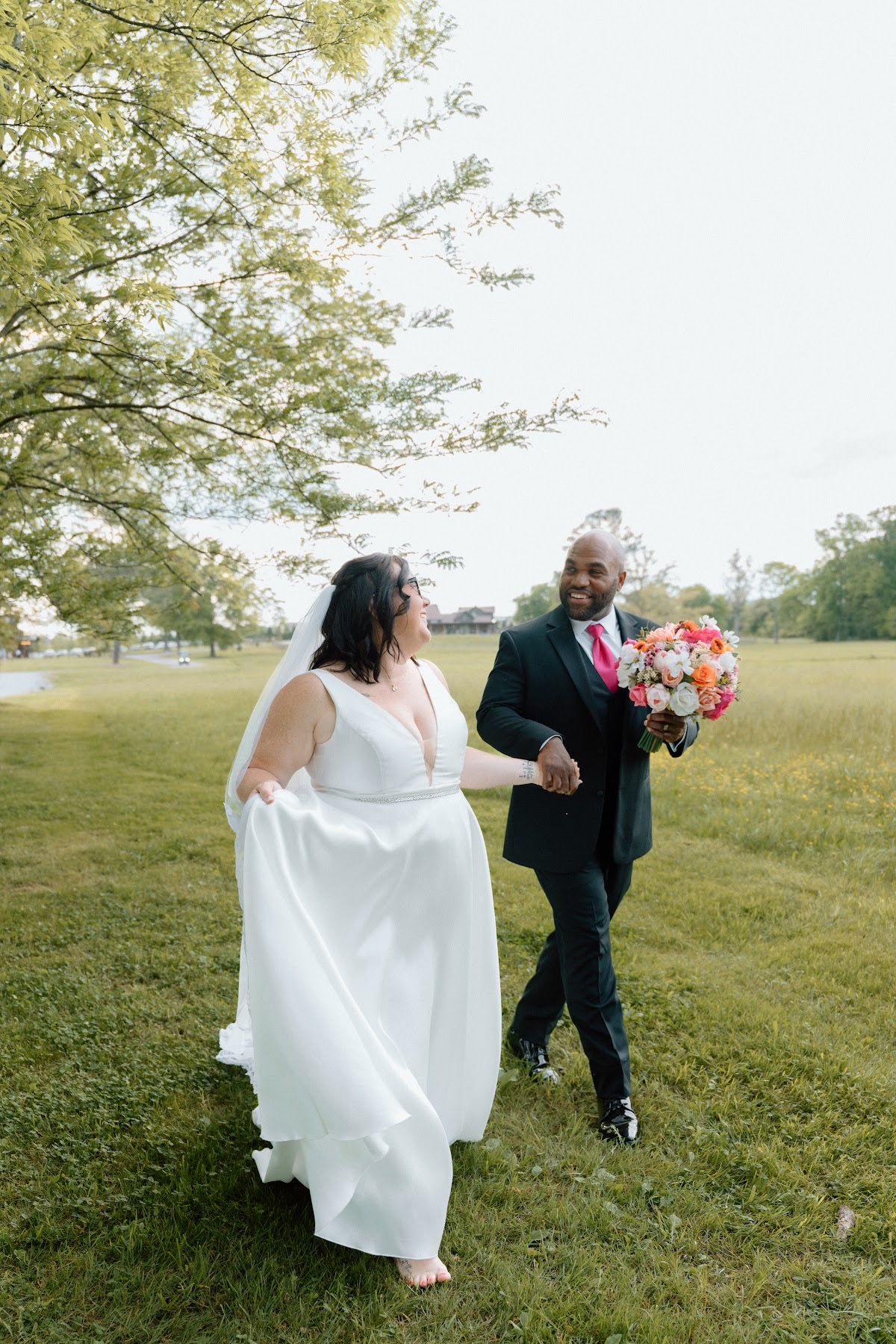 Stephanie & Josh smile while walking hand in hand across the lawn toward the barn at Covey Creek