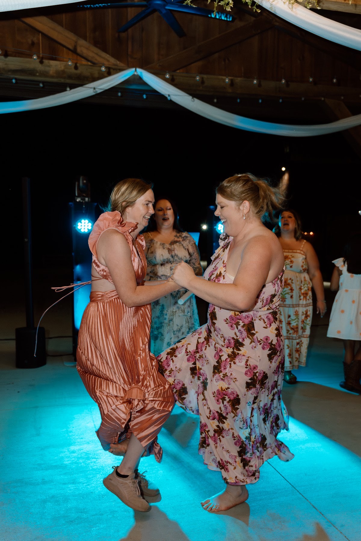 Guests in copper and pink dresses dance under blue light at Stephanie & Josh's Covey Creek reception