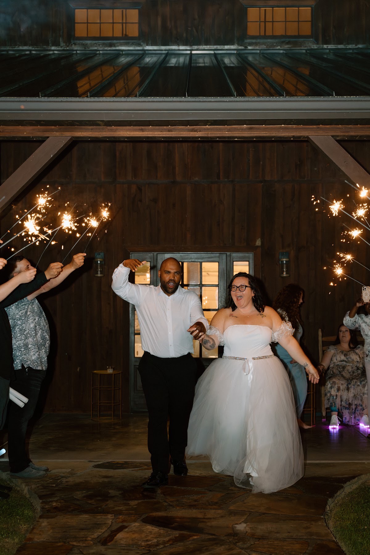 Stephanie & Josh cheer hand in hand through a sparkler tunnel outside the barn at Covey Creek