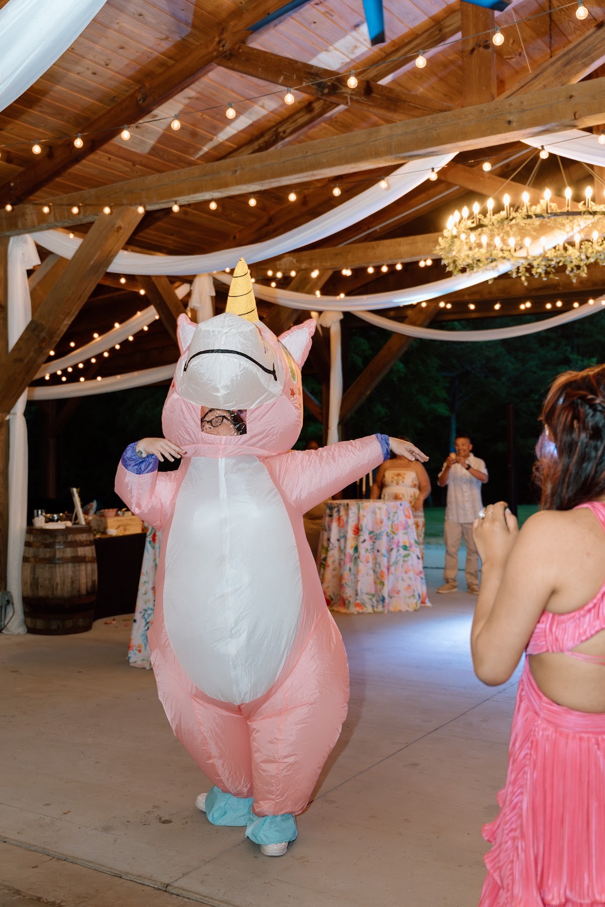 A guest in a pink inflatable unicorn dances under pavilion string lights for Stephanie & Josh at Covey Creek